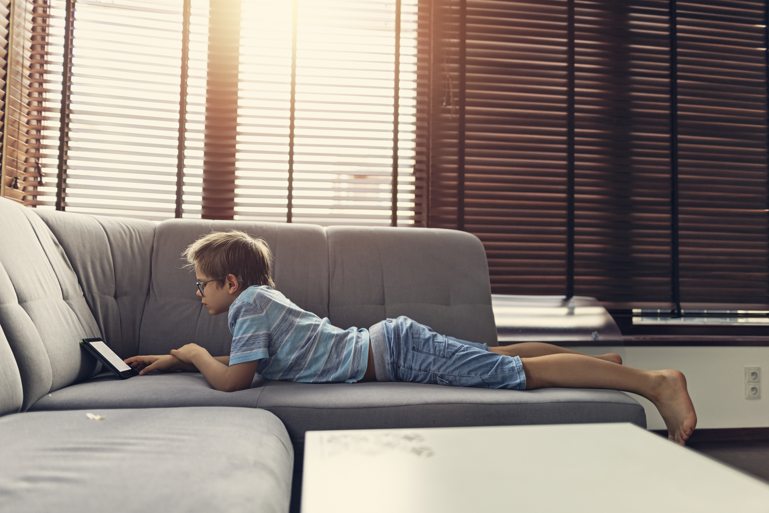 boy reading e-reader under blinds